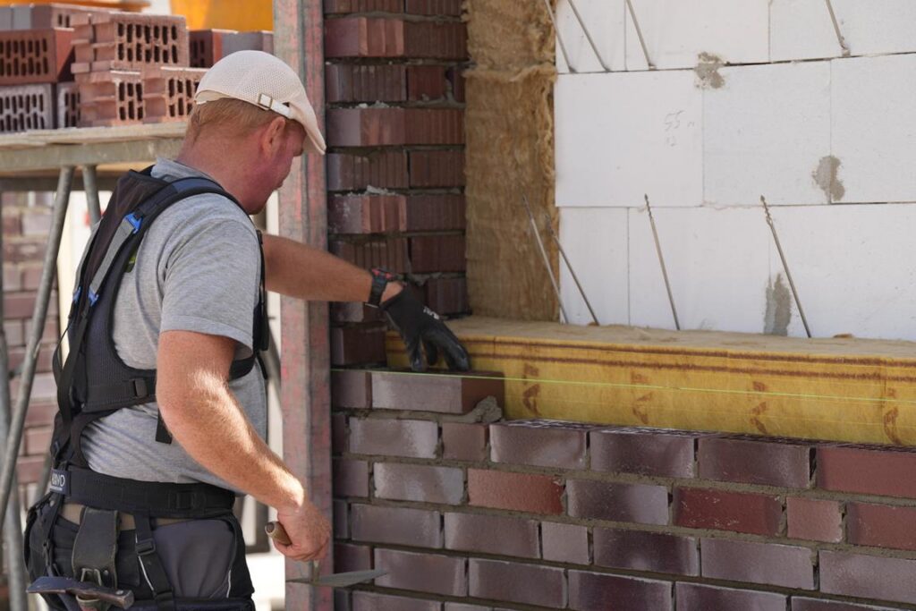 Handwerker beim Verlegen von Ziegeln an einer Baustelle, mit Fokus auf präzise Mauerarbeiten und Verwendung von Mauerwerkzeug.